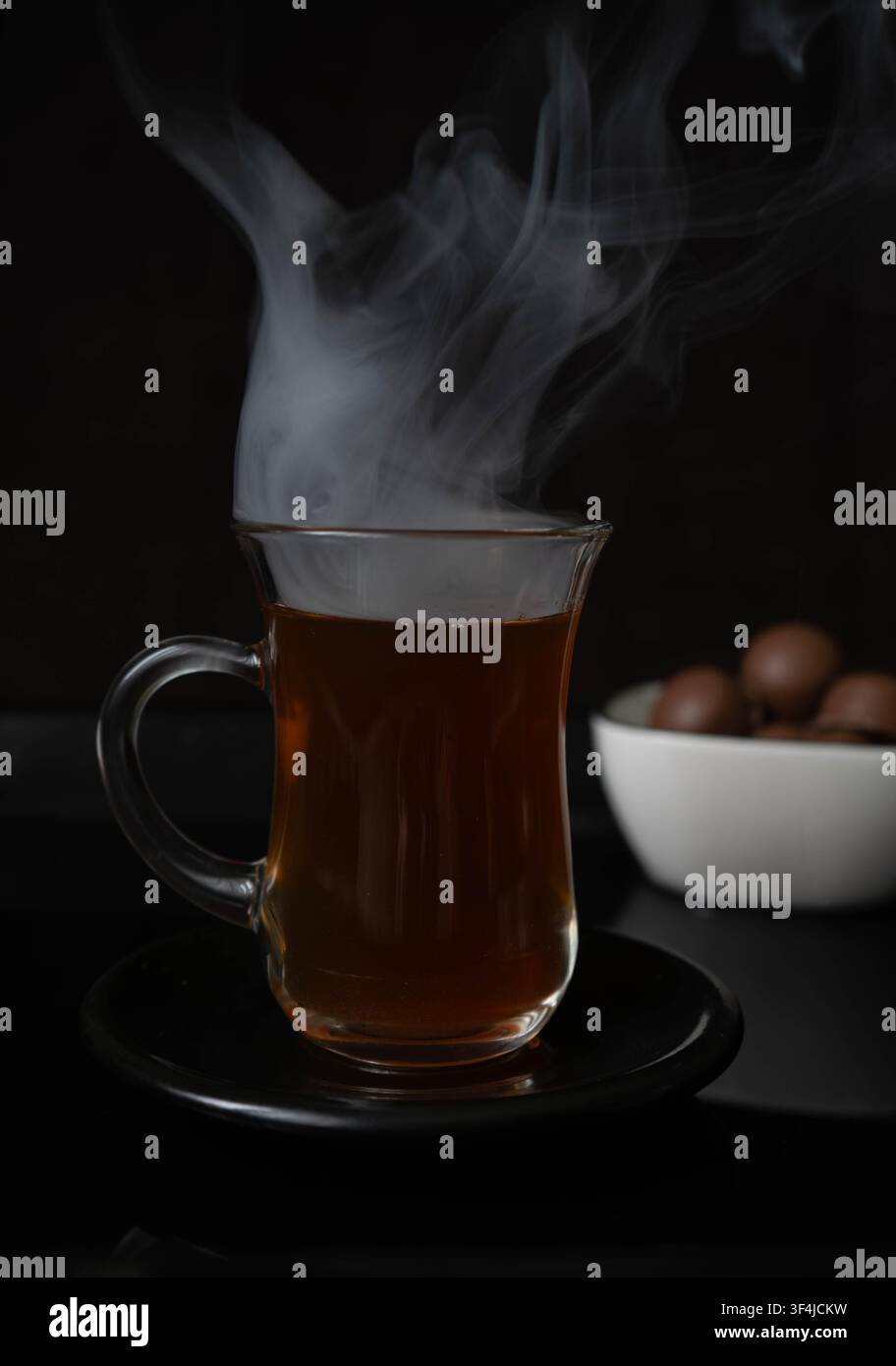 Heißer schwarzer Tee, serviert in einer traditionellen Glastasse mit dramatischem Dampf auf dunklem Hintergrund. Konzept für ein gemütliches warmes Getränk. Stockfoto