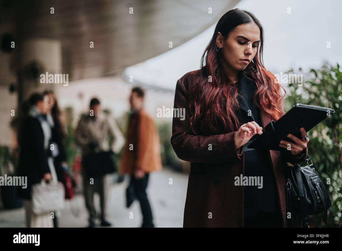 Geschäftsperson verwendet ein Tablet außerhalb des Büros, während Kollegen im unscharfen Hintergrund warten Stockfoto