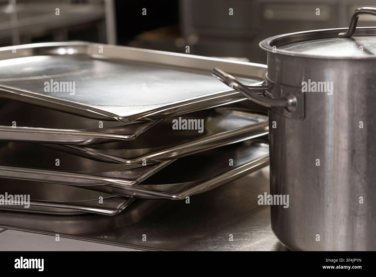 Nahaufnahme von ordentlich angeordneten Edelstahlblechen und einem Topf mit reflektierenden Oberflächen. Stockfoto