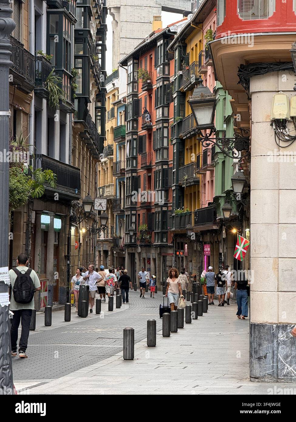 Belebte enge Straße gesäumt von farbenfrohen traditionellen Balkonen in der Altstadt von Bilbao, Baskenland, Spanien. - Smartphone-aufgenommenes Stockfoto