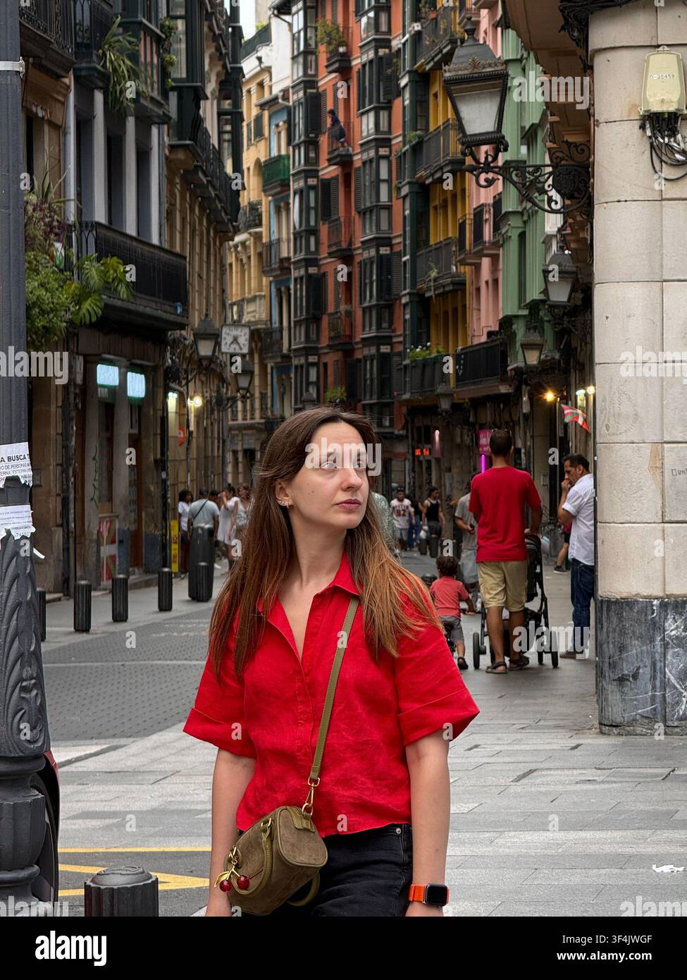 Frau in einem roten Hemd geht durch eine belebte Straße in der Altstadt von Bilbao, Baskenland, Spanien. - Smartphone-aufgenommenes Stockfoto