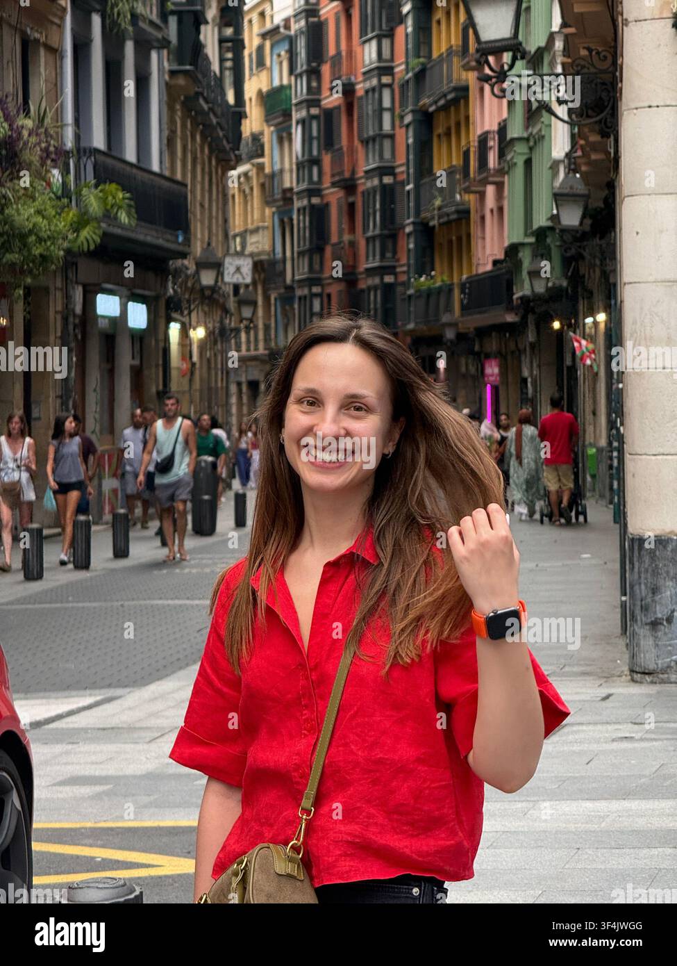 Frau in einem roten Hemd geht durch eine belebte Straße in der Altstadt von Bilbao, Baskenland, Spanien. - Smartphone-aufgenommenes Stockfoto