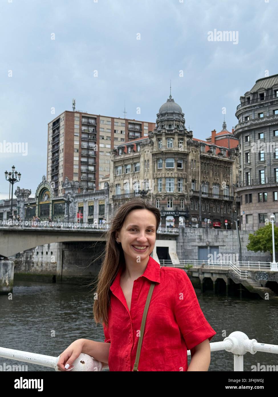 Frau in einem roten Hemd, die am Nervión-Fluss im Zentrum von Bilbao im Baskenland, Spanien, posiert. - Smartphone-aufgenommenes Stockfoto