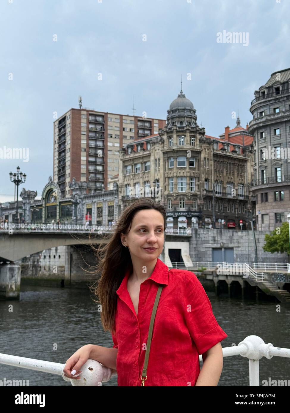 Frau in einem roten Hemd, die am Nervión-Fluss im Zentrum von Bilbao im Baskenland, Spanien, posiert. - Smartphone-aufgenommenes Stockfoto