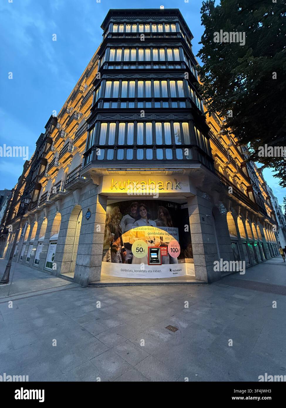 Beleuchtete Kutxabank-Filiale in einem verzierten Eckgebäude zur Blauen Stunde in Bilbao, Spanien. - Smartphone-aufgenommenes Stockfoto