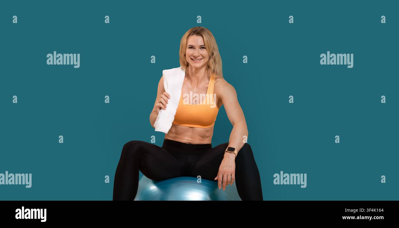 Entspannen Sie sich nach dem Heimtraining. Lächelnd muskulöse Frau mittleren Alters in Sportkleidung mit Handtuch auf der Schulter Stockfoto