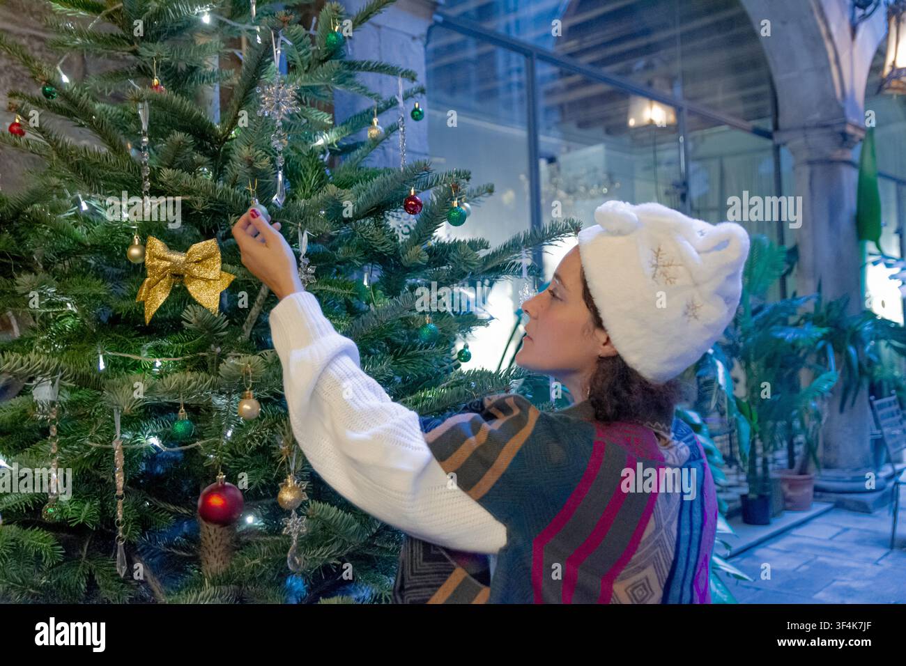 Frau dekoriert Weihnachtsbaum mit Ornamenten und trägt Wintermütze Stockfoto