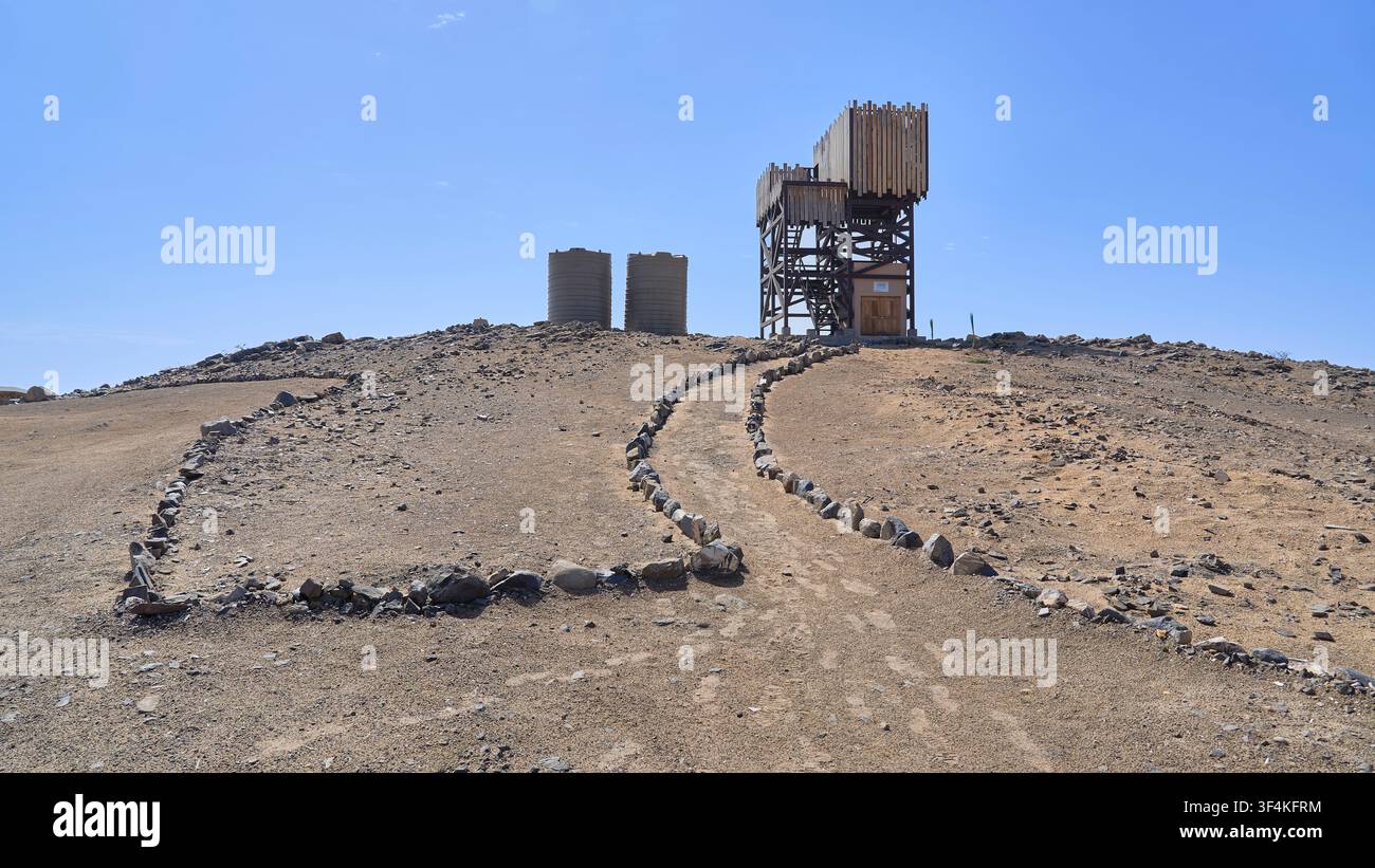 Ein hölzerner Aussichtsturm und Wassertanks befinden sich auf einem felsigen, trockenen Hügel mit einem steinernen Weg am Eingang des Skeleton-Coast-Nationalparks. Stockfoto
