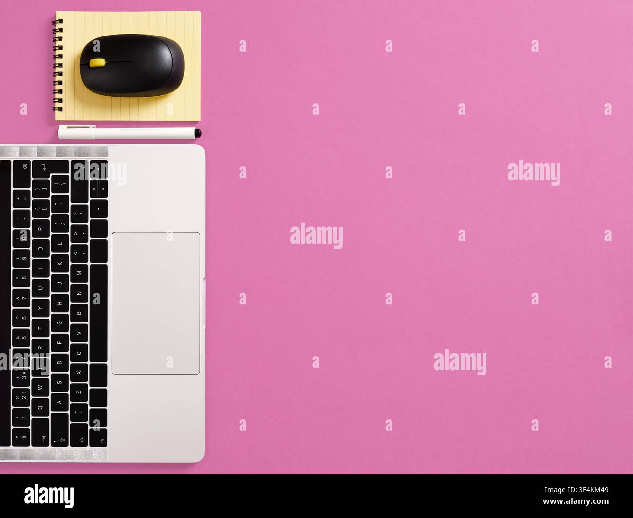 Arbeitsplatz mit Laptop-Tastatur, Maus, gelbem Notizblock und Stift, die auf einem lebhaften rosa Hintergrund mit Kopierplatz angeordnet sind Stockfoto