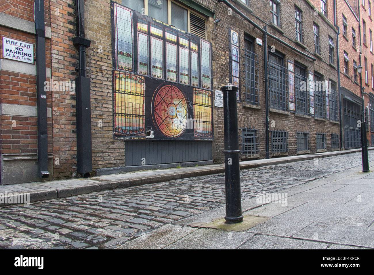 Schmale historische Kopfsteinpflasterstraße mit Backsteingebäuden, die große Drucke von Buntglasfenstern in Dublin, Irland, zeigen Stockfoto