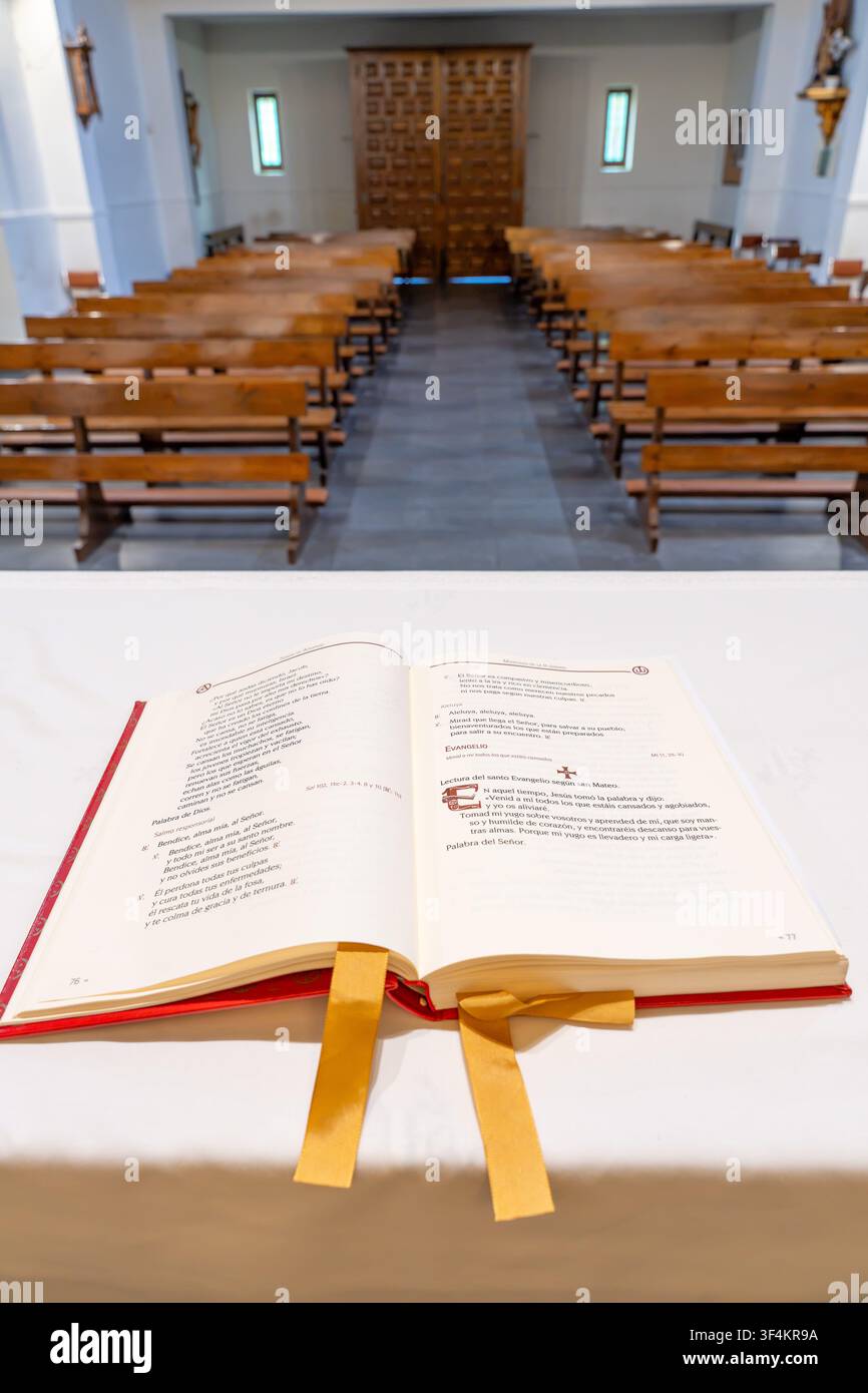 Offenes Messbuch, das auf dem Altar ruht, mit Kirchenbänken im Hintergrund, symbolisch für Glauben und Anbetung Stockfoto