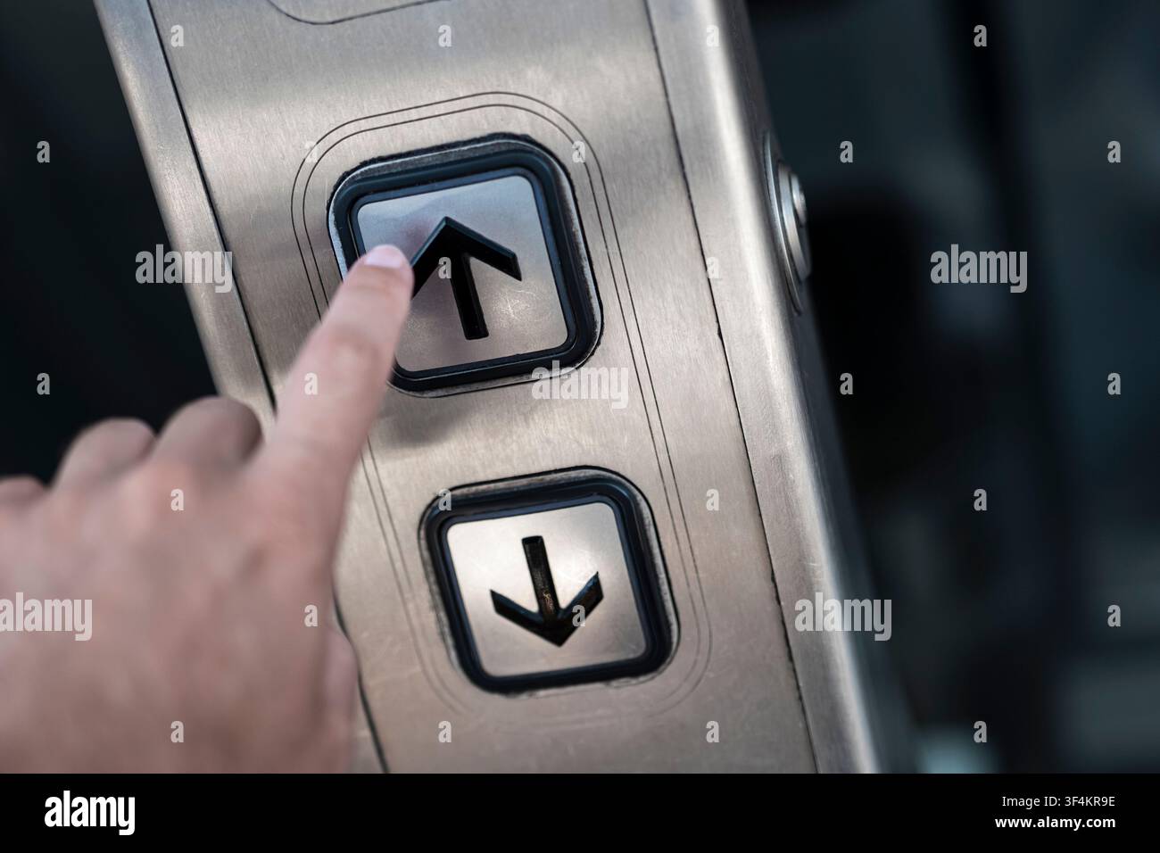 Finger drückt eine NACH-OBEN-Taste auf einem Fahrstuhlschalter, die moderne Verkehrsinfrastruktur und vertikale Mobilität veranschaulicht. Stockfoto