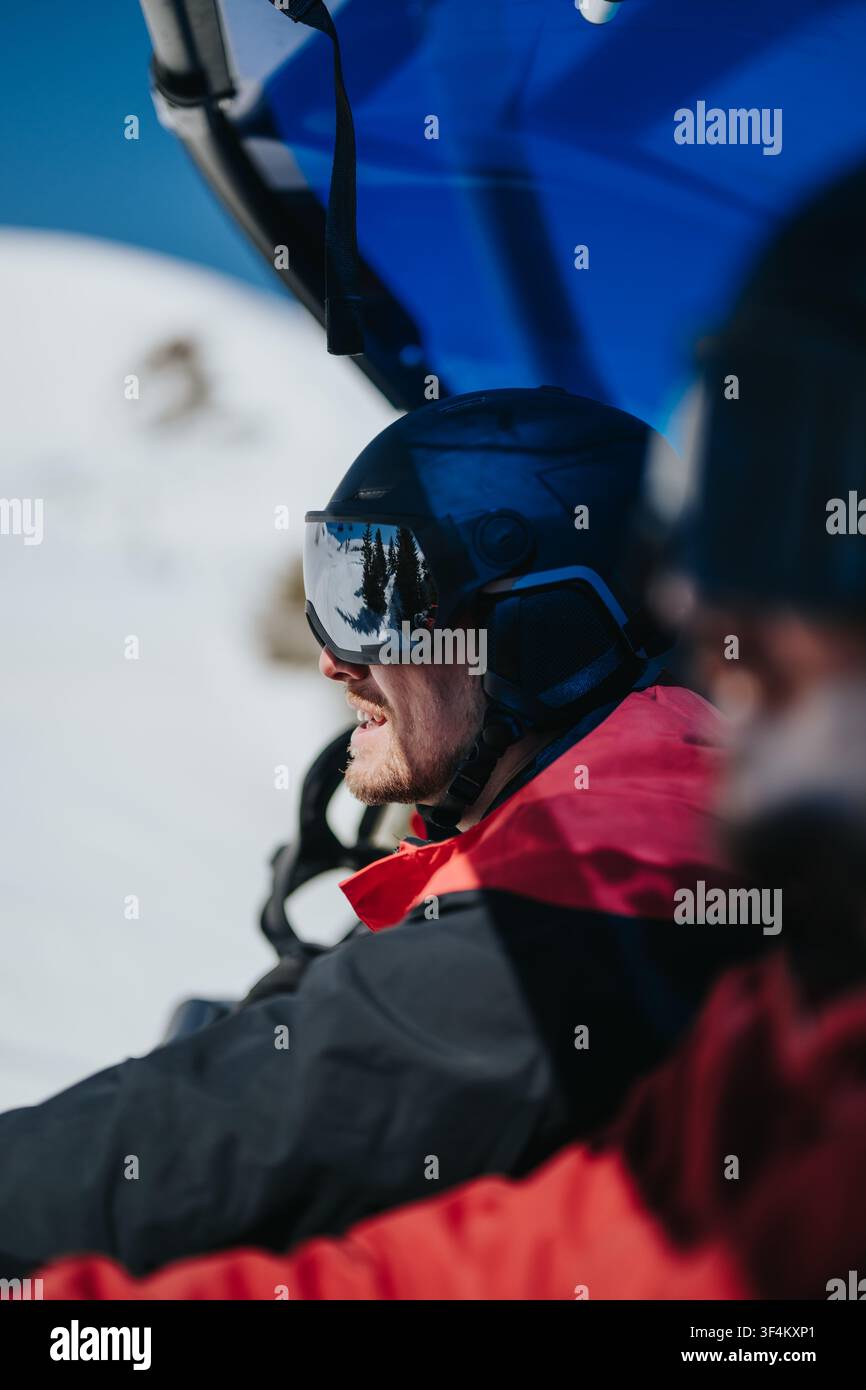 Mann mit Helm und Schutzbrille auf dem Skilift, der auf die schneebedeckte Berglandschaft schaut Stockfoto