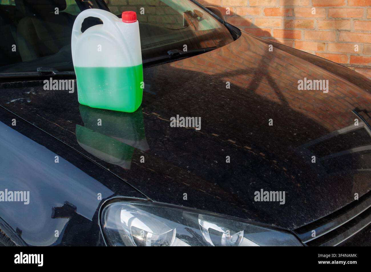 Grüne Flüssigkeit in einem Plastikbehälter auf einer staubigen schwarzen Motorhaube Stockfoto