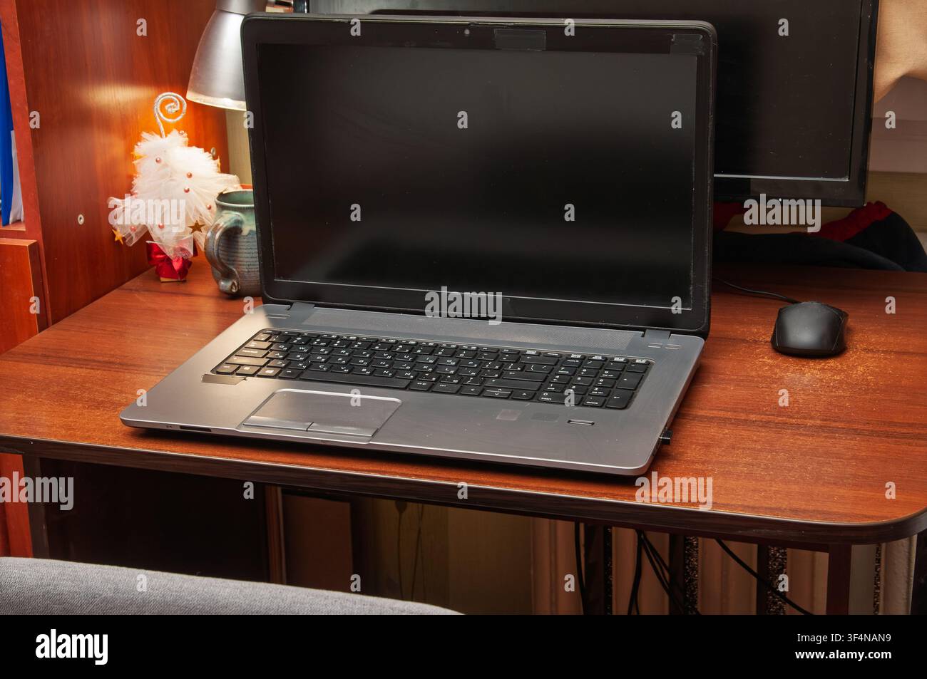 Ein Laptop und eine Computermaus stehen auf einem Holzschreibtisch mit einer Lampe und einem Dekoartikel Stockfoto