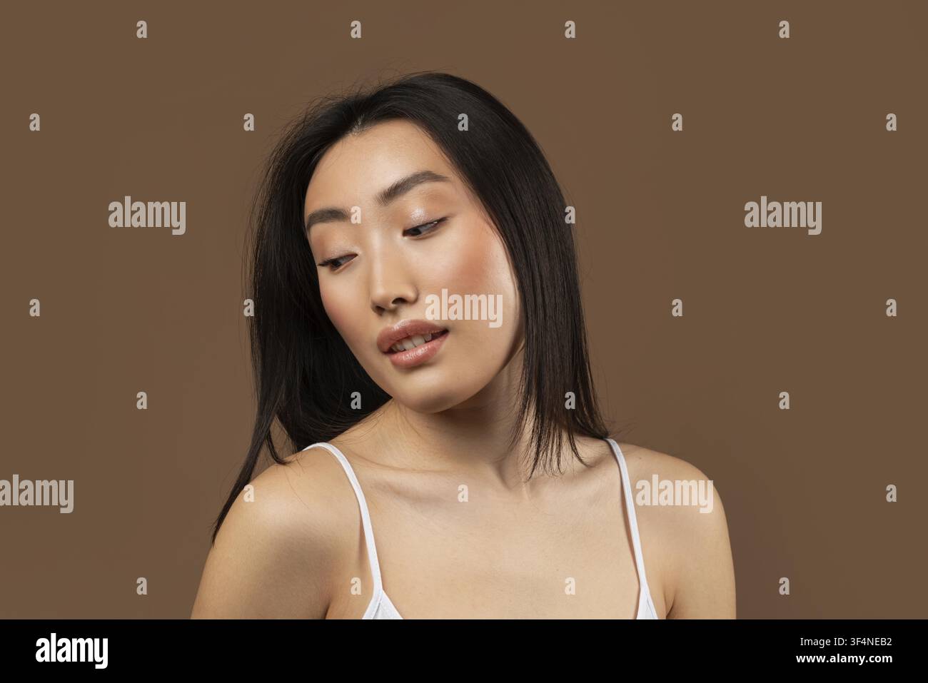 Junge asiatische Frau posiert mit nachdenklichem Ausdruck, brauner Hintergrund Stockfoto