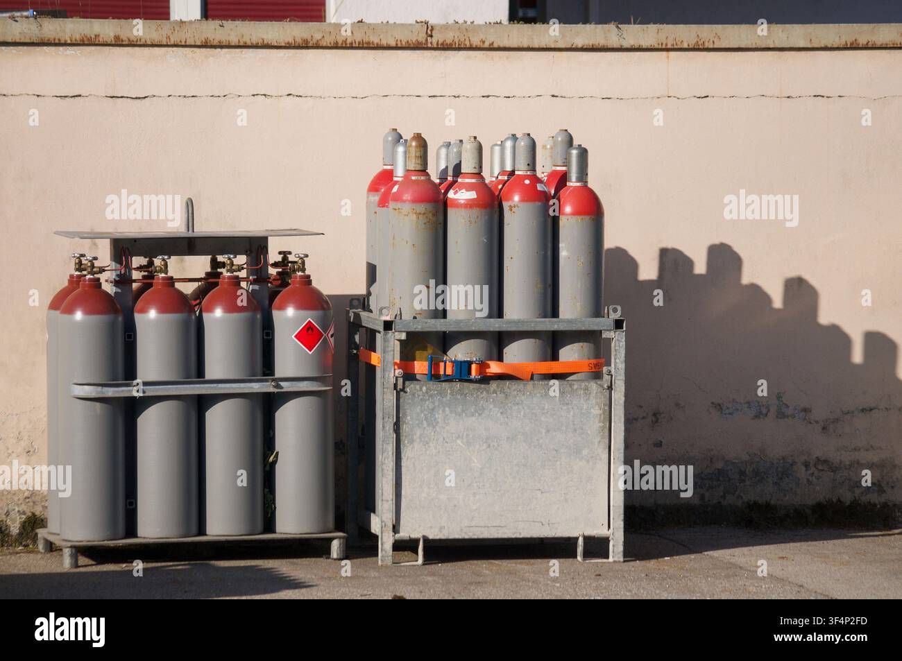 Frontansicht von industriellen Druckgasflaschen, die in Metallpaletten und Gestellen außerhalb einer Anlagewand gelagert sind. Hochdruckgasflaschen Stockfoto
