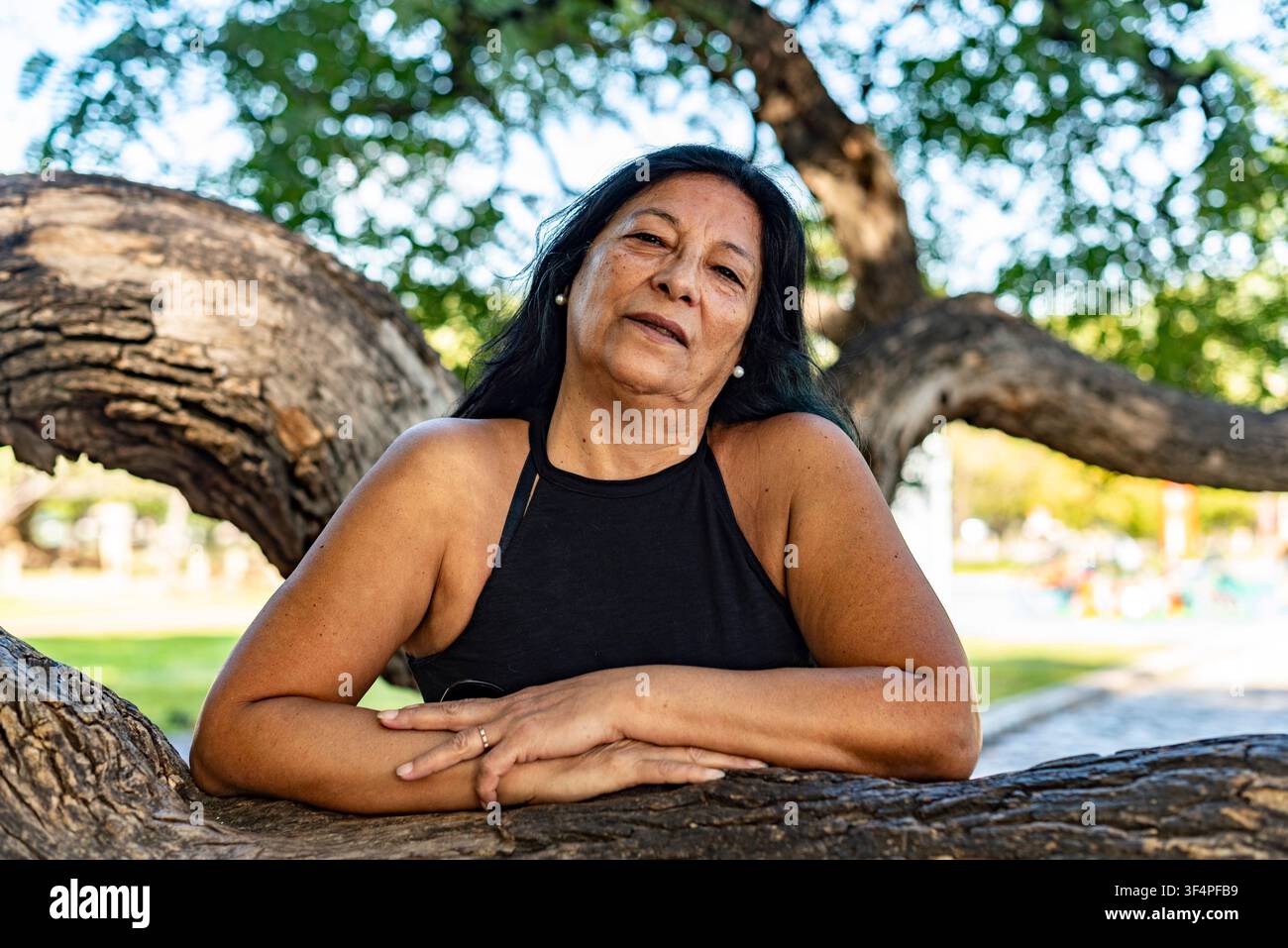 Sanfter Blick einer reifen südamerikanischen Frau, die sich bequem gegen einen großen alten Baum lehnt Stockfoto