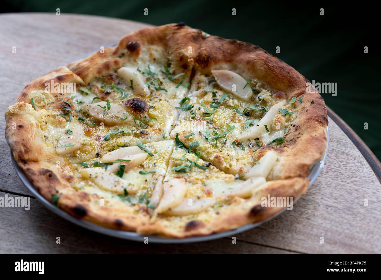 Leckere Pizza mit Scheiben frischer Birne, Kräutern und einem Tropfen Sauce, serviert auf rustikalem Holz. Stockfoto