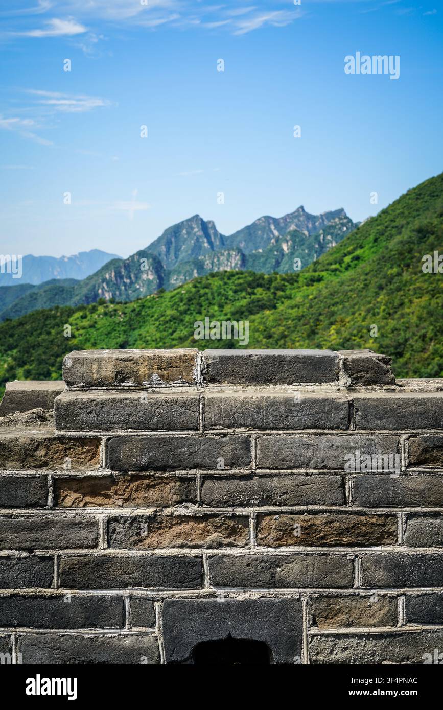 Eine strukturierte graue Steinmauer mit sichtbarem Mörtel und einigen bräunlich-orangenen Ziegeln füllt die unteren zwei Drittel des Bildes und zeigt verwitterte Details. Ab Stockfoto