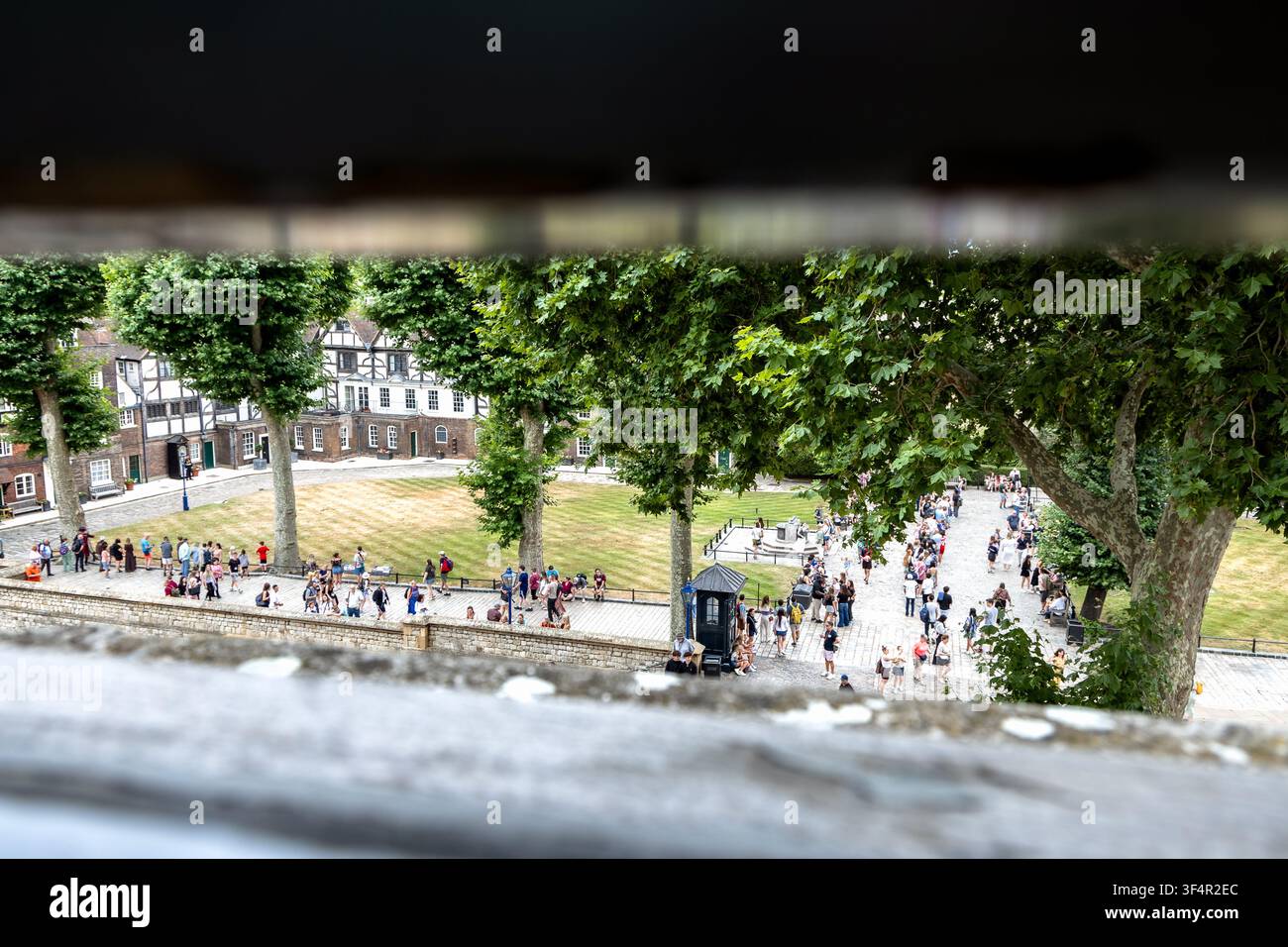 London, England, UK - 14. Juli 2026: Besucher erkunden den Inneren Burghof des Tower of London, wie durch ein schmales Fenster vom White Tower aus gesehen Stockfoto