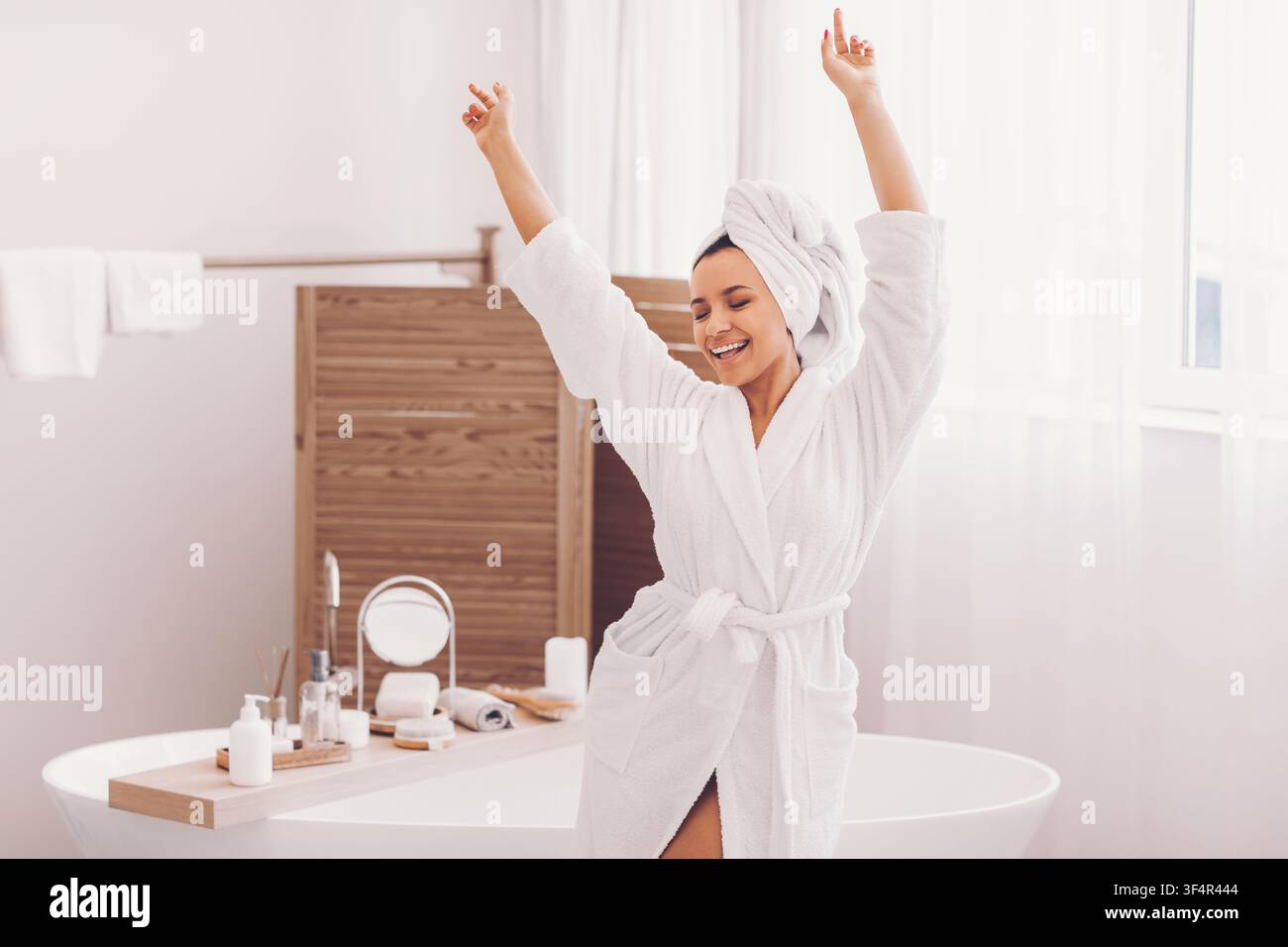 Glückliche Frau genießt ihre Morgenroutine in weißem Bademantel und Handtuch, Badezimmer, Wellness-Konzept Stockfoto