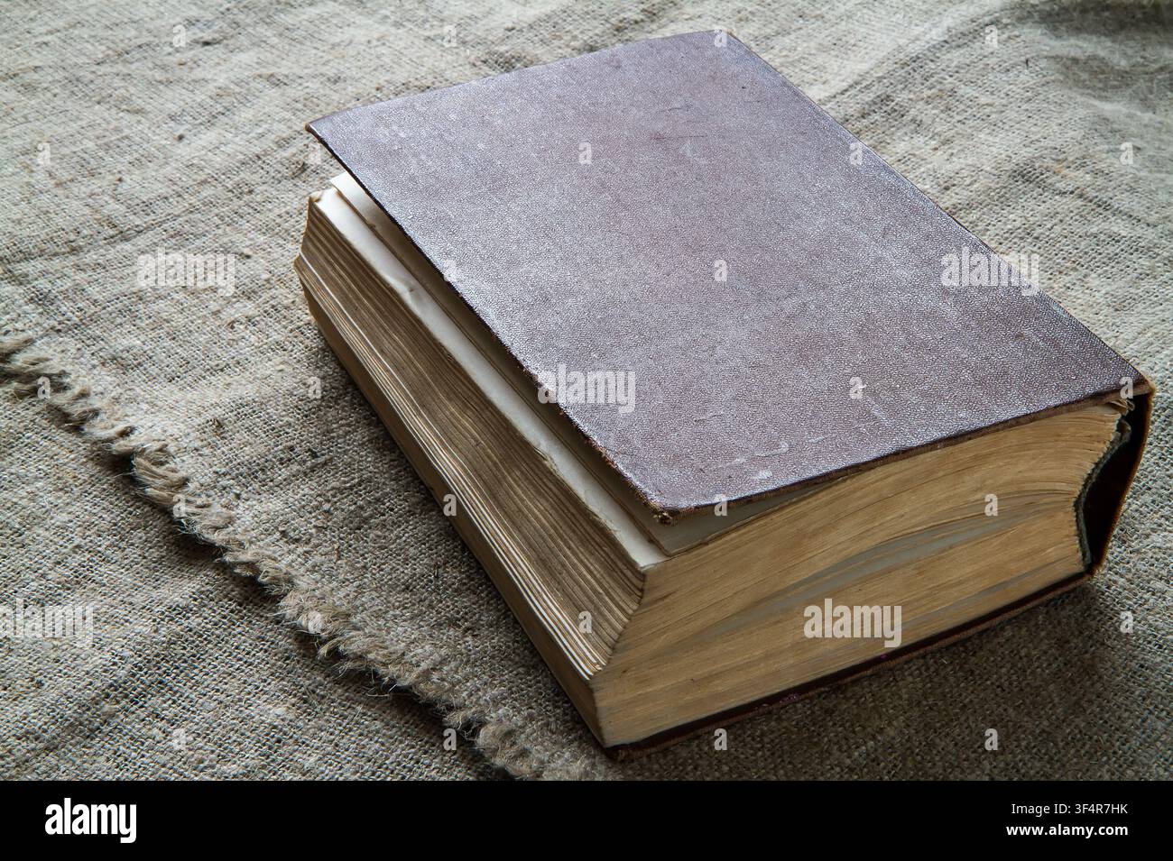Ein altes Buch vor einem Hintergrund aus rauer Stoff. Ein Buch mit vergilbten Seiten in einem braunen Ledereinband. Stockfoto