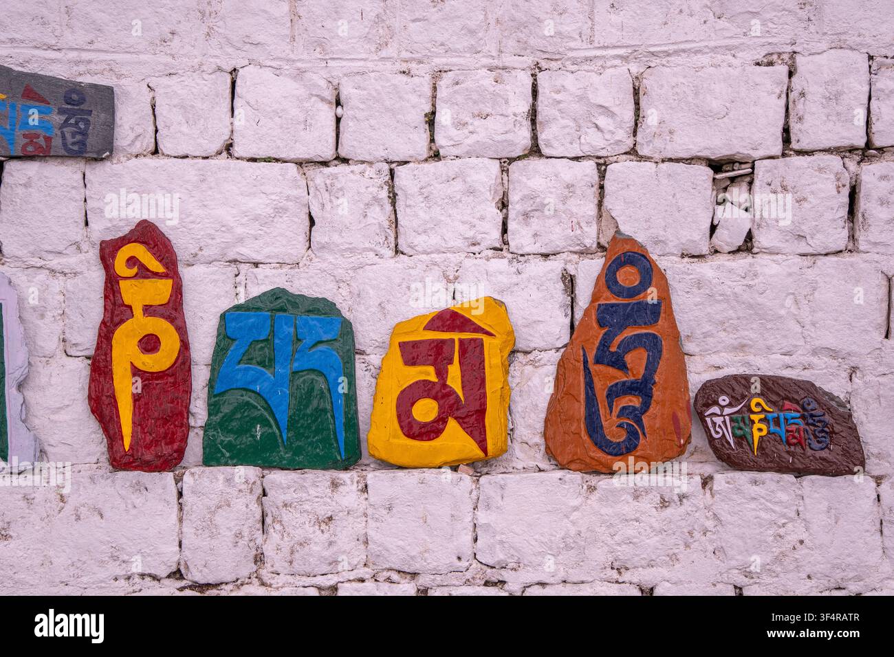 Hellfarbene Steine, die mit dem Mantra „Om mani padme hum“ graviert sind, vor einer Wand aus weißen Steinen angeordnet. Dharamsala, Himachal Pradesh, Indien Stockfoto