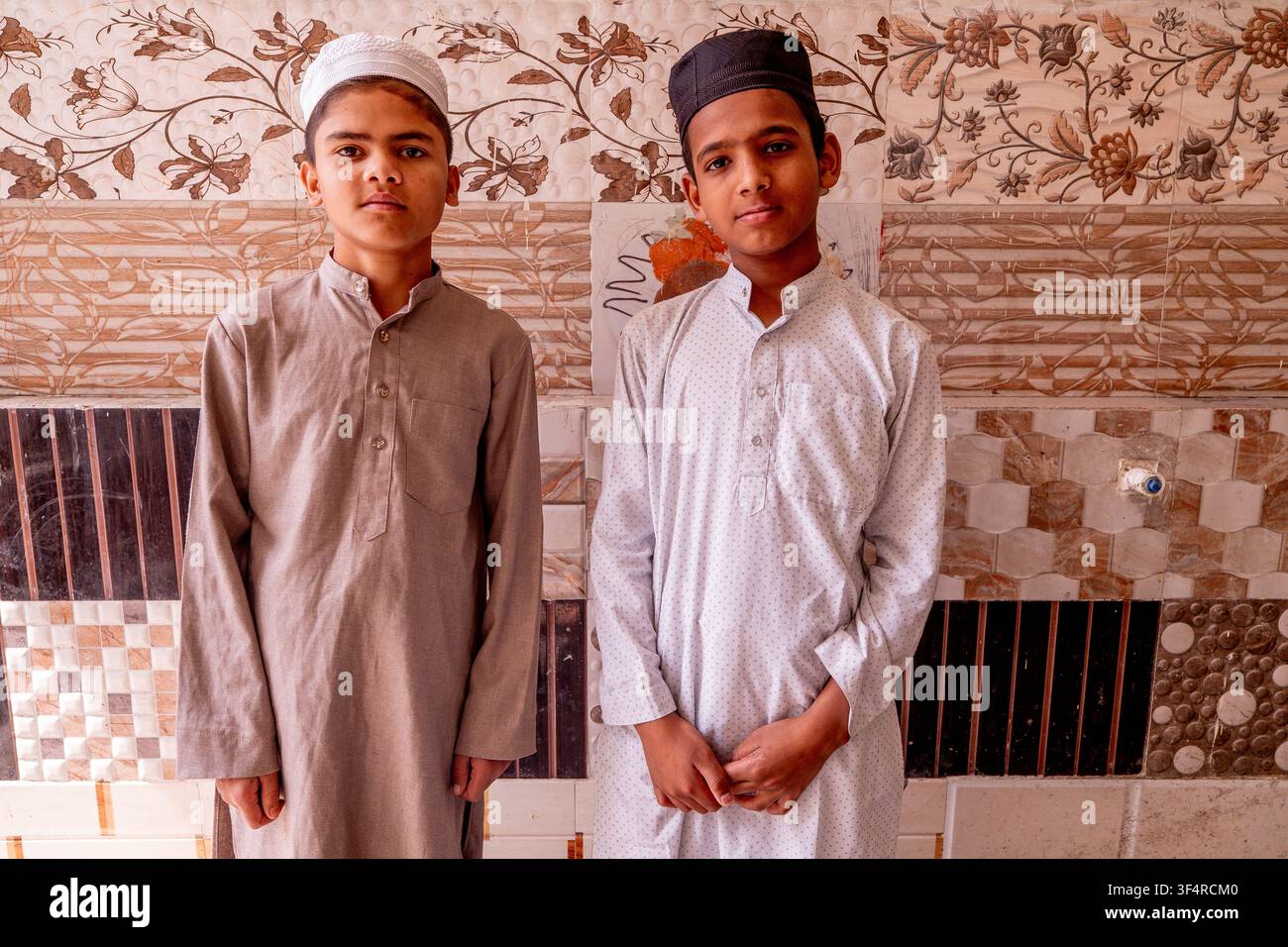 Zwei Jungen in Kurta und Taqiyah stehen vor einer Wand mit Blumenmustern und dekorativen Fliesen in der Jama Masjid Khairuddin Grand Moschee Stockfoto