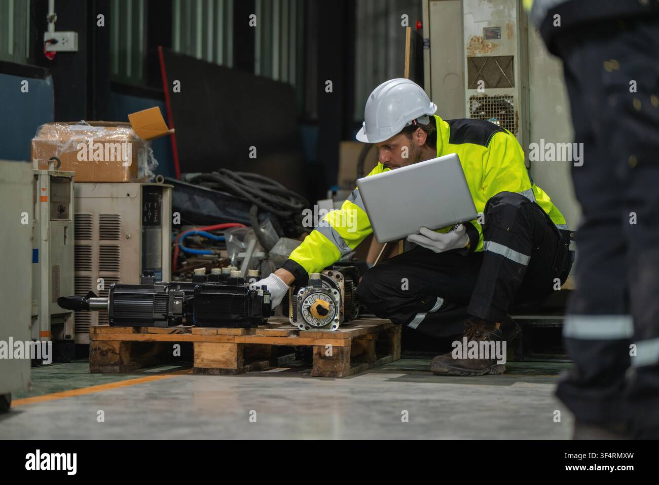 Industrieingenieure mit Laptop in der Hocke, die Maschinenteile Servomotorenteile eines Roboterarms auf einer Palette in der Fabrik inspizieren. Konzept des Lagerkontrolls Stockfoto