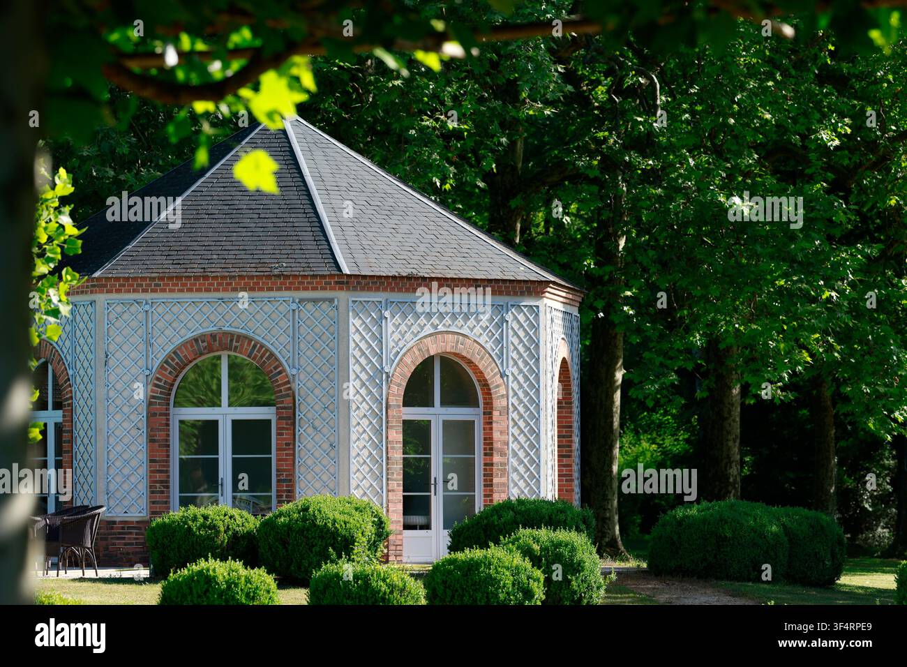 Ein Gartenpavillon mit einem Ziegeldach und gewölbten Fenstern, umgeben von Grün und Bäumen. Stockfoto