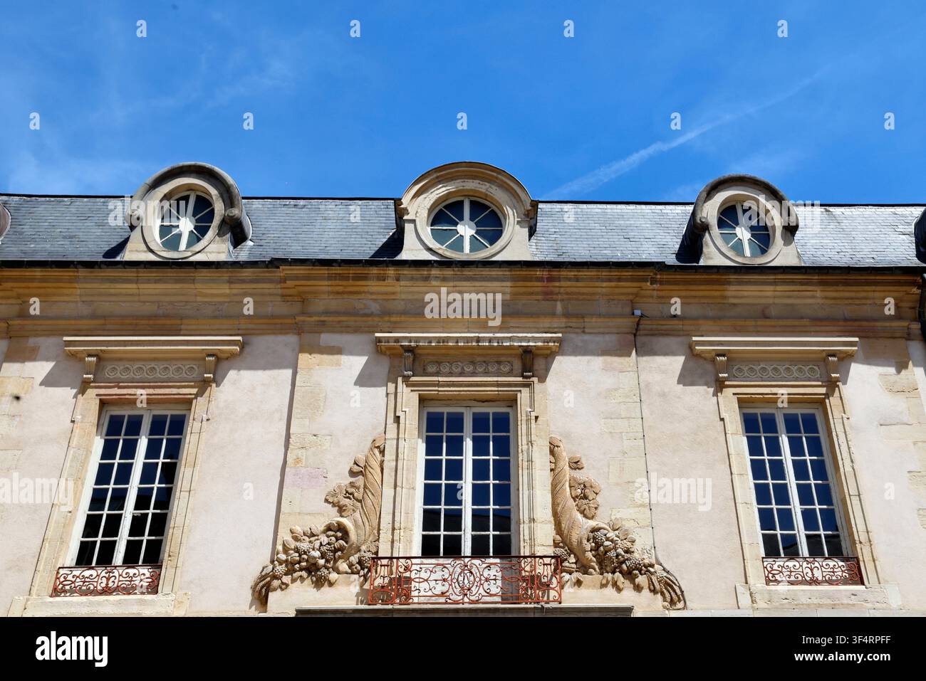 Architektonisches Detail eines Herrenhauses: steinerne Bullauge-Fenster, ein Gesims mit Modillionen, französische Fenster mit verzierten Geländern und Basreliefs von Füllhörnern Stockfoto