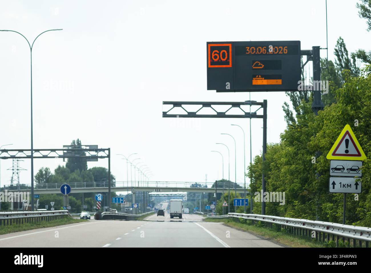 Moderne Autobahn mit überhead elektronischem Schild, das Geschwindigkeitsempfehlungen und Reisehinweise anzeigt, während der Verkehr darunter an einem hellen Tag fließt und intelligente i illustriert Stockfoto