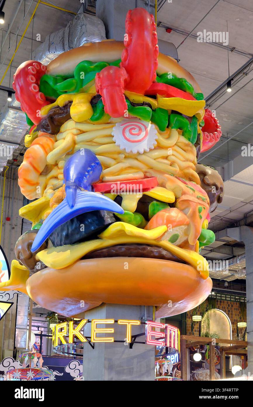 Ein lebhaftes Einkaufszentrumsinnere mit bunten Neonschildern, einer riesigen Burger-Dekoration und einer Vielzahl von Restaurants, die asiatische Küche und Fast Food anbieten. Stockfoto