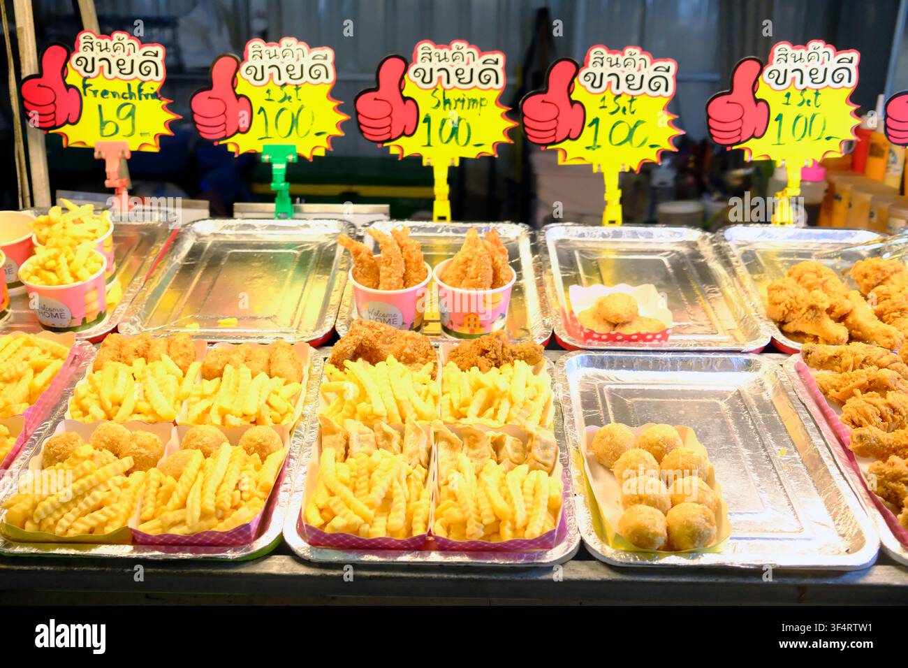 Ein Straßenimbiss bietet eine Vielzahl von frittierten Speisen wie Pommes frites, Garnelen und Brathähnchen an, wobei die Preise in thailändischen Baht angegeben sind. Bangkok, Thaila Stockfoto