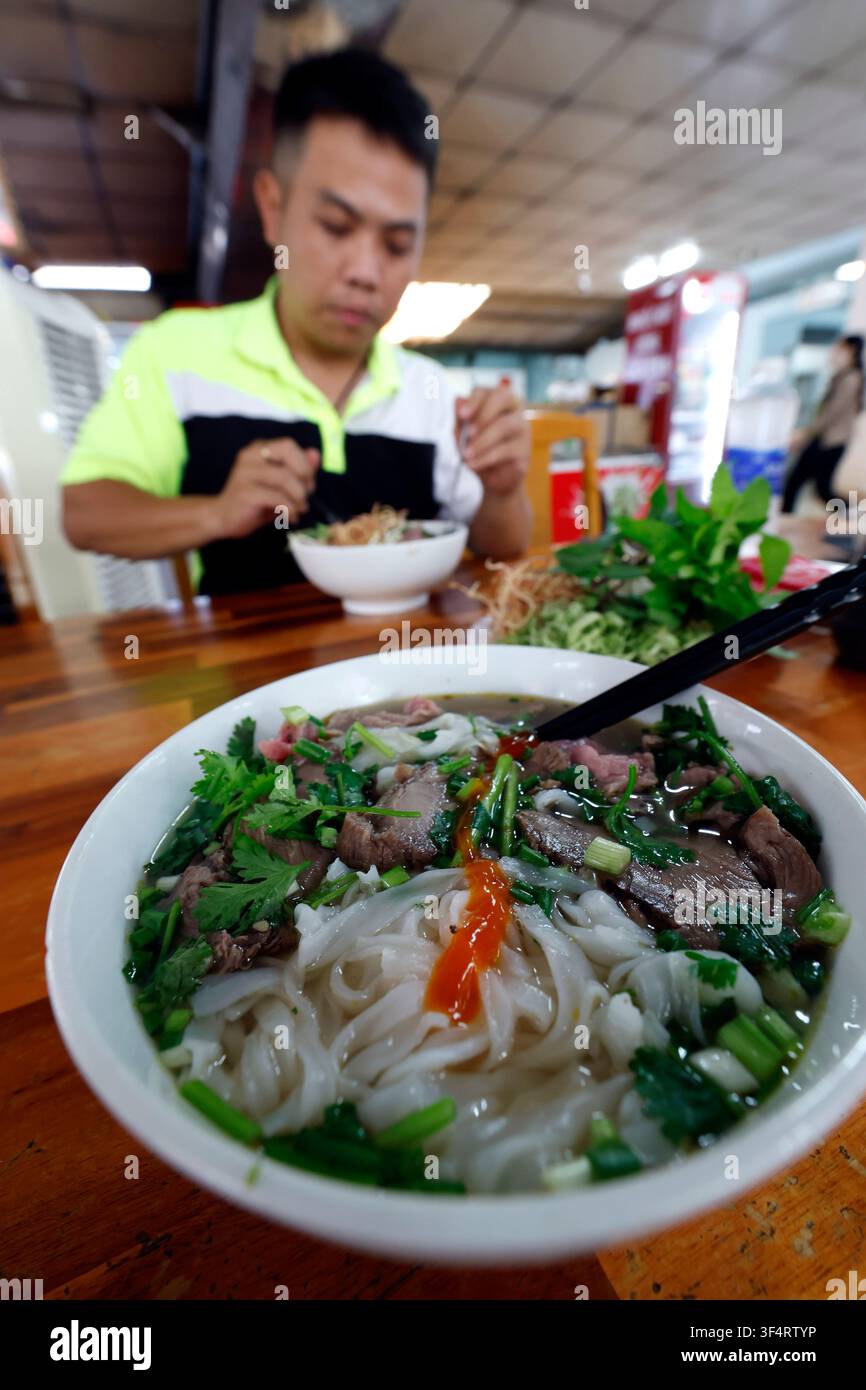 Ein Mann genießt eine Schüssel Pho, ein traditionelles vietnamesisches Gericht, in einem lokalen Restaurant. Nudeln, Fleisch und frische Kräuter machen dieses ikonische Gericht aus. Ho Chi Minh Stockfoto