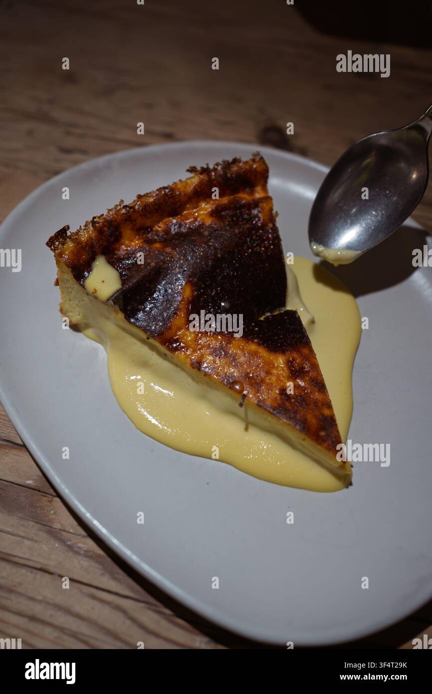 Basisch gebrannter Käsekuchen, serviert mit cremiger Vanillecreme auf einem Teller Stockfoto