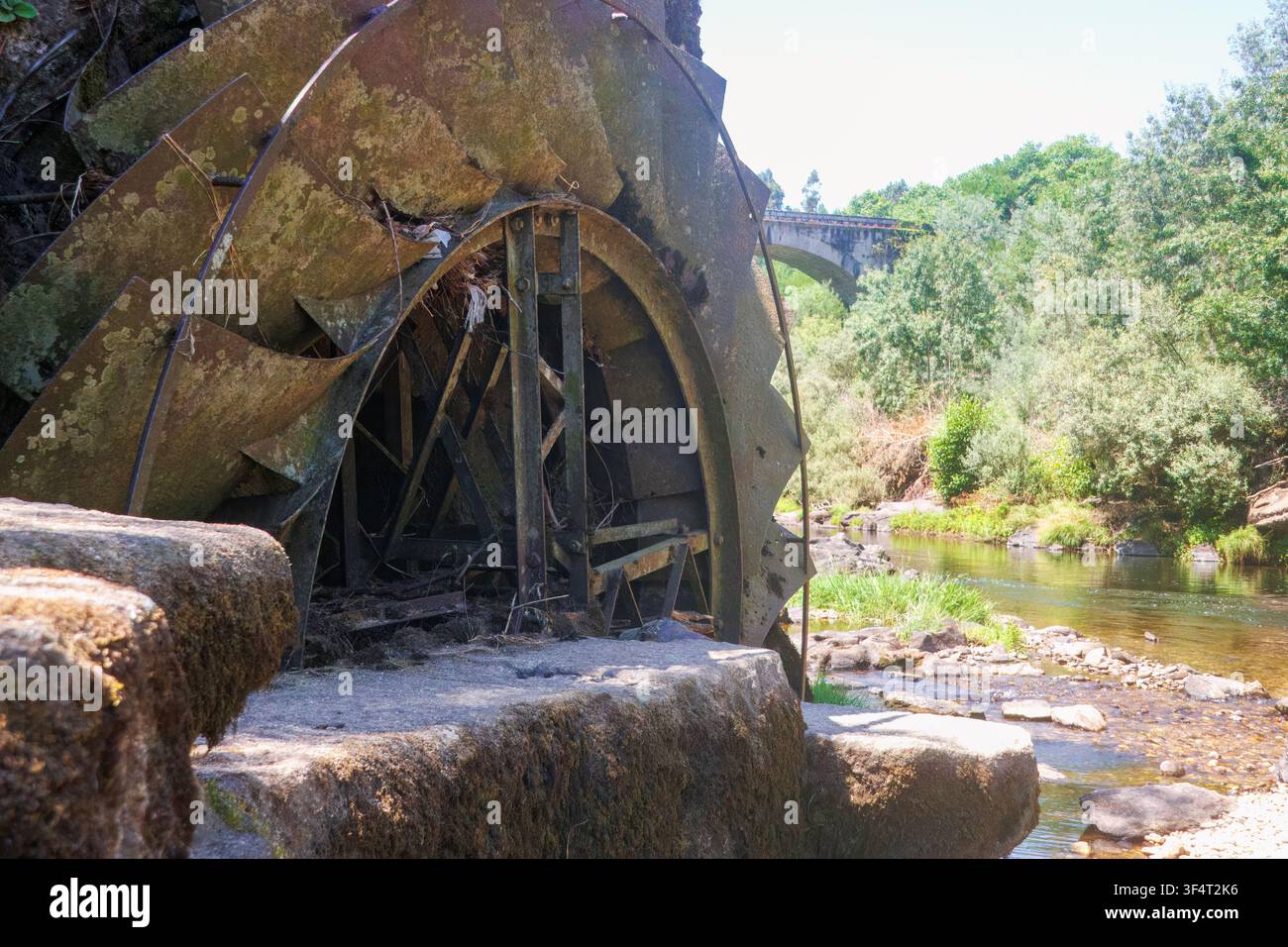 Nahaufnahme einer alten verrosteten Metall-Wasserradstruktur, die zu einer alten Mühle am felsigen Ufer des Flusses Tamega in Portugal gehört. Stockfoto