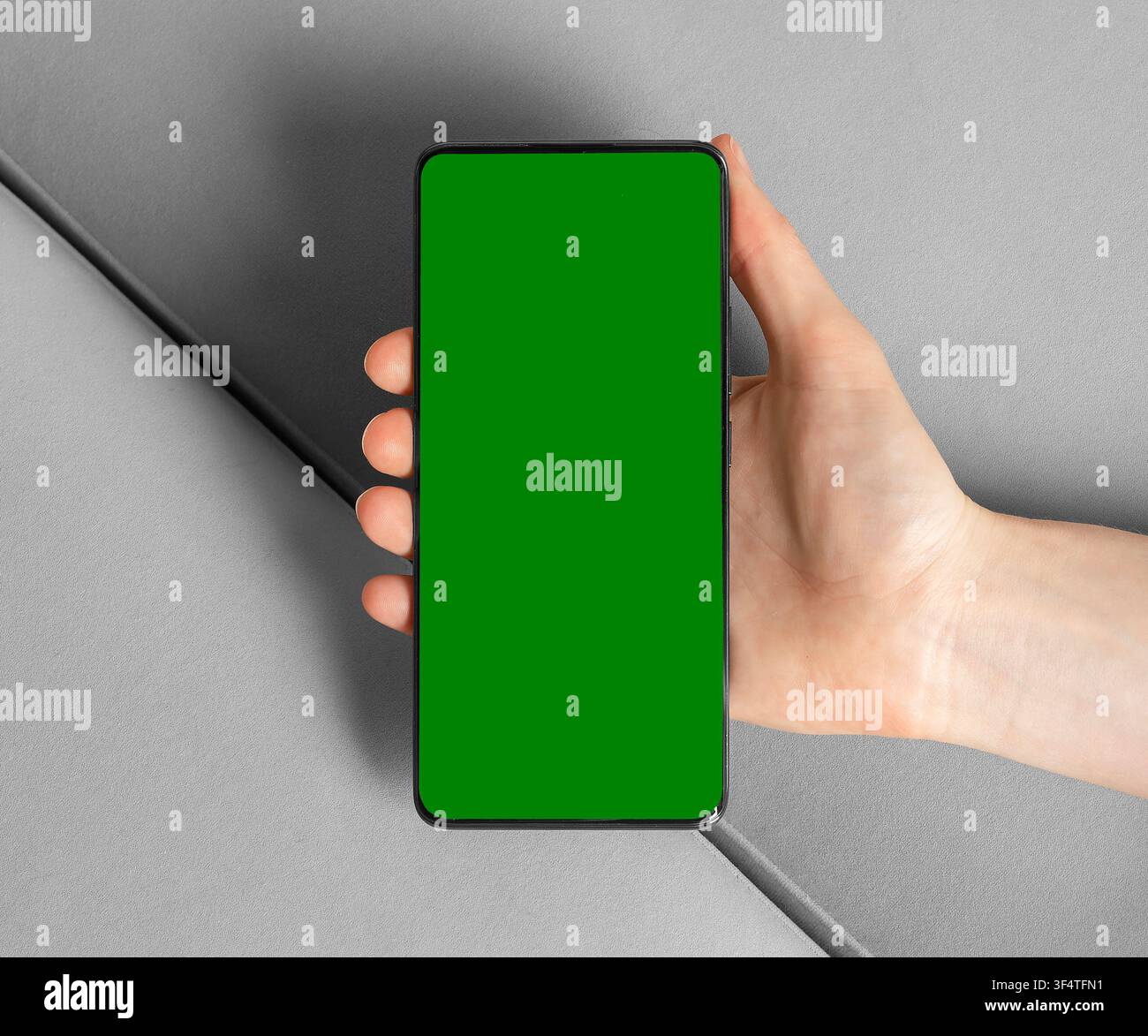 Hand hält Smartphone mit grünem Bildschirm. Handy-Mockup auf grauem Hintergrund. App-Werbung und UI-Design-Vorlage. Stockfoto