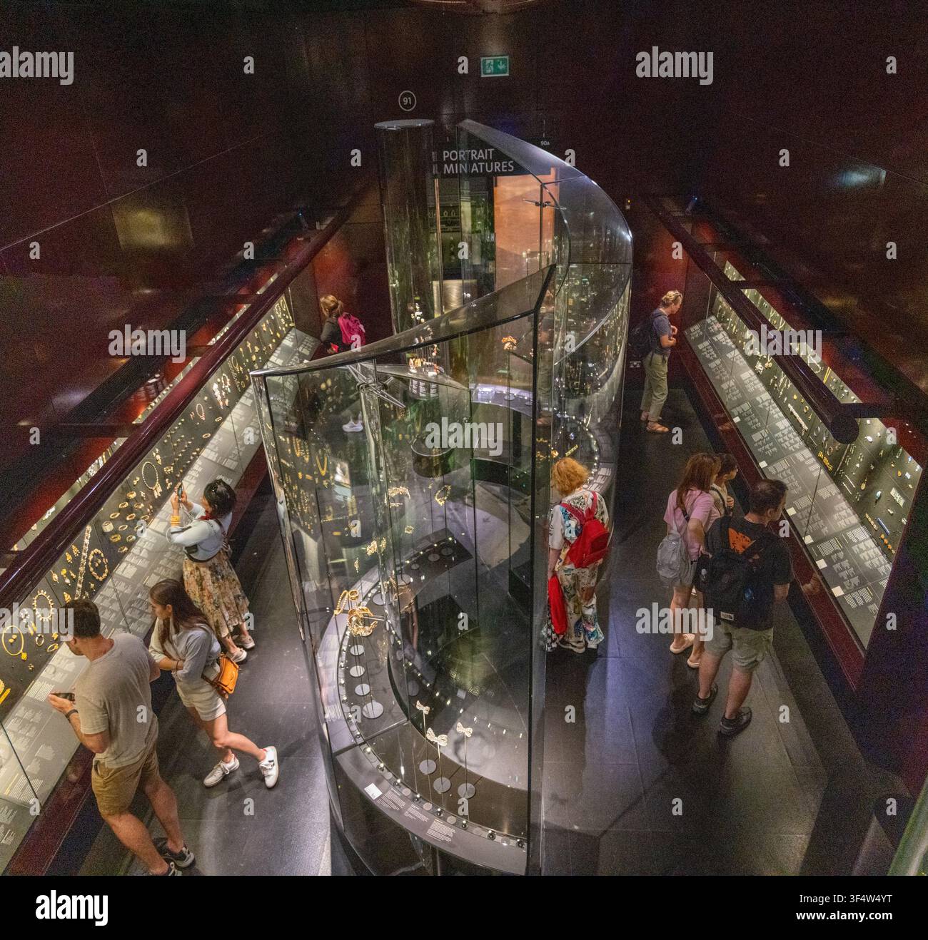 London, UK - 26. Jun 25: Besucher erkunden beleuchtete Schmuckausstellungen in einer dunklen Galerie im Victoria and Albert Museum in London. Stockfoto