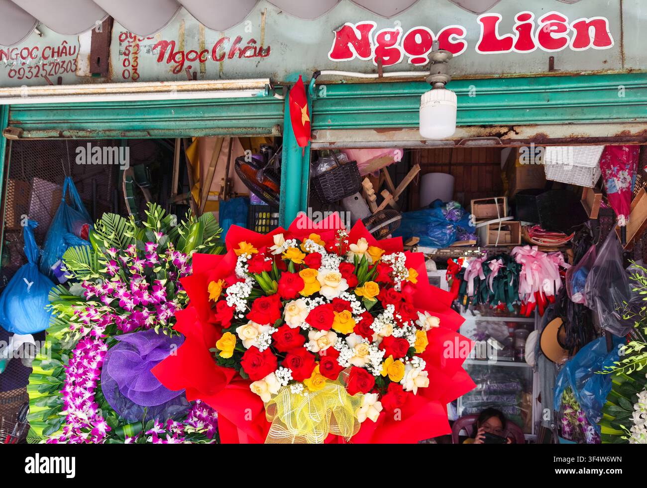 Han Market oder Cho Han, Blumenladen namens „Ngọc Liên“, mit einem lebendigen roten und gelben Blumenstrauß, der neben lila Orchideenarrangements verpackt ist. Stockfoto