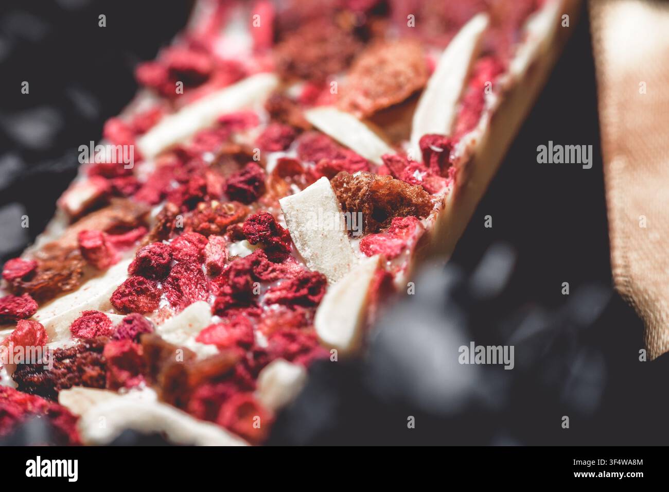 Nahaufnahme einer handgefertigten weißen Kunstschokoladenriegel mit großzügigen Mengen getrockneter Himbeeren und kleinen Stückchen von Nüssen oder anderen Einbänden Stockfoto