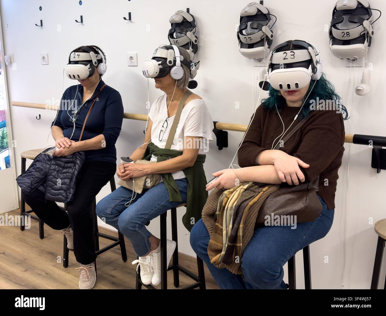 Drei sitzende Frauen tragen Virtual-Reality-Headsets und Kopfhörer in einem gemeinsamen immersiven Technologieraum. Stockfoto