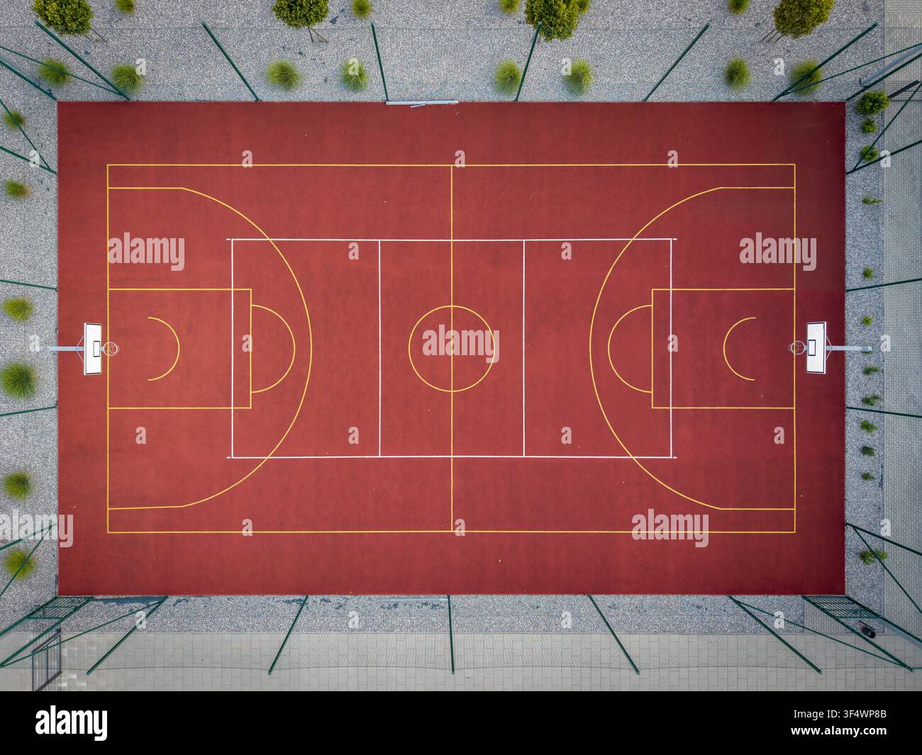 Luftaufnahme eines roten Basketballplatzes mit gelben Linien, umgeben von einem Zaun und kleinen grünen Büschen in Krakau, Woiwodschaft Kleinpolen, Polen. Stockfoto