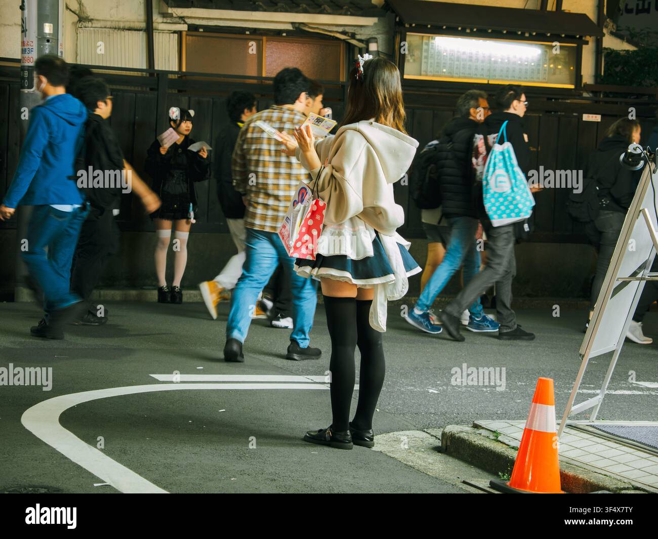 Fußgänger gehen nachts auf einer Straße in Tokio, Japan, mit einer Frau in einem Cosplay-Outfit, die am Bürgersteig steht Stockfoto