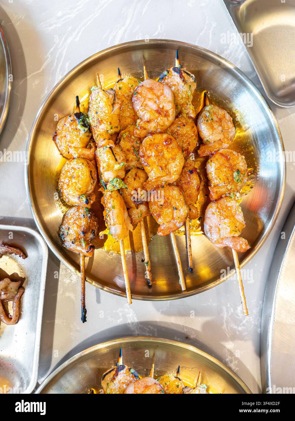 Gegrillte Garnelen-Spieße, die auf einem runden goldenen Metallteller in einem traditionellen koreanischen BBQ-Restaurant serviert werden. Stockfoto