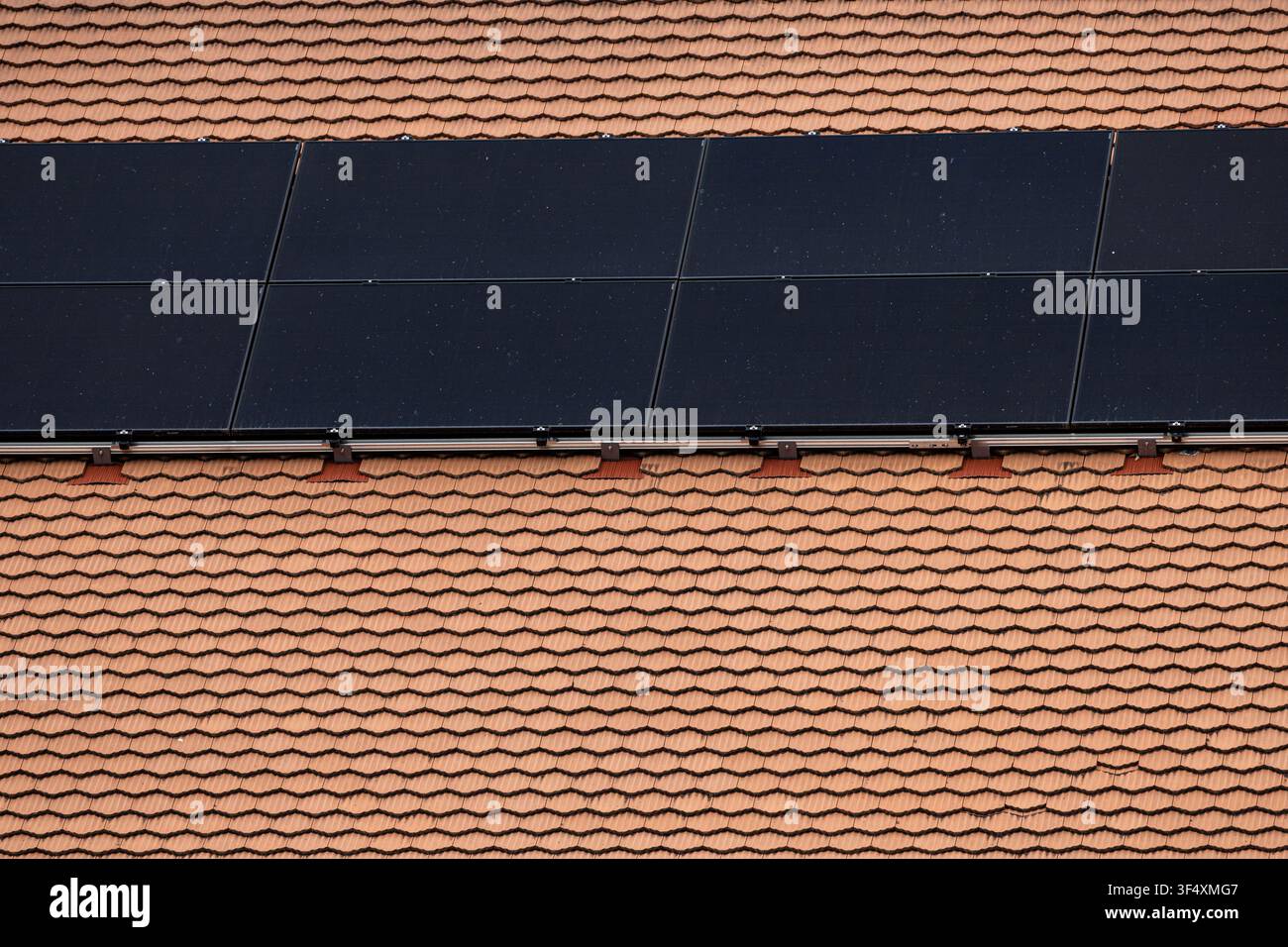 Solarphotovoltaikpanele, die auf einem Ziegeldach einer Wohngebäude installiert sind, produzieren erneuerbare Energie in der Schweiz. Stockfoto