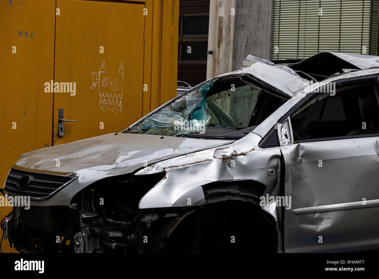 Beschädigtes silbernes Personenkraftfahrzeug mit schweren Frontschadenschäden, geparkt in einem Industriegebiet. Verkehrsunfall und Verkehrssicherheitskonzept. Stockfoto
