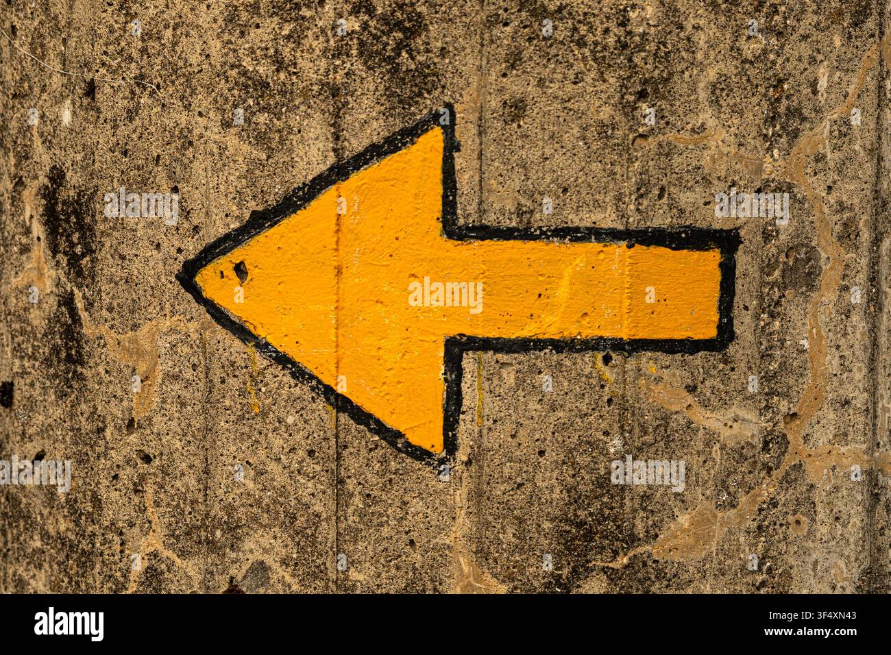 Gelbe Richtungs Pfeil auf einer verwitterten Betonoberfläche, der nach links zeigt, Nahaufnahme eines urbanen Wegweiser-Symbols. Stockfoto