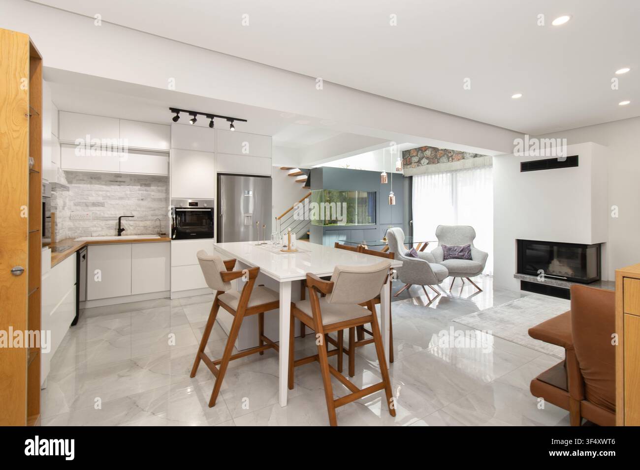 Modernes Loft-Style Wohn- und Esszimmer mit Kücheninsel und hölzernen Barhockern, eingebautem Kamin und Aquariums-Element Stockfoto